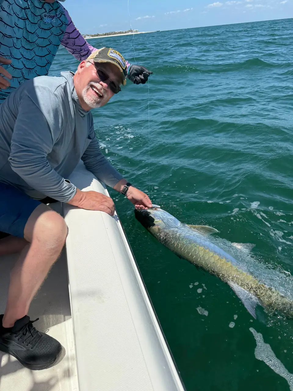 Smiling angler with a tarpon in the water beside the boat.