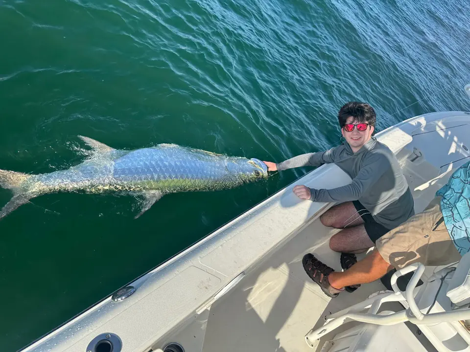 Angler holding a large tarpon alongside the charter boat.