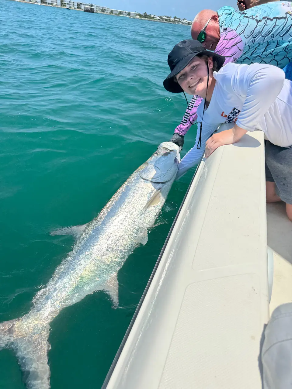 Angler and guide beside a large tarpon in the water alongside the boat.