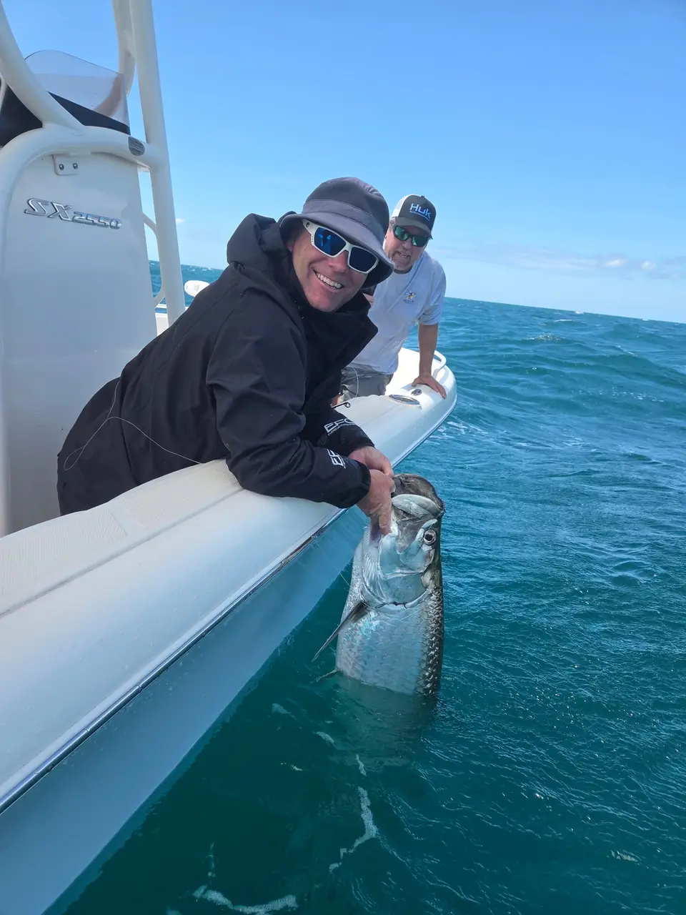 Two anglers posing with a tarpon alongside the boat.
